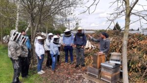 Imkerkurs26 Rückblick auf den Grundkurs 2021. Kursleiter am offenen Bienenstock und neun KursteilnehmerInnen am Standort der Gärtnerei Böckenkamp.